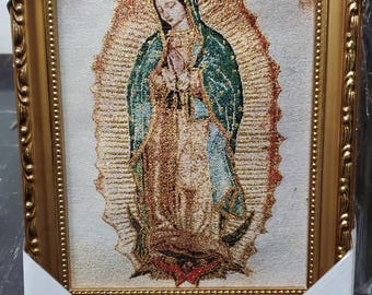 May include: Gold-framed tapestry depicting the Virgin of Guadalupe. The artwork features a detailed image of the Virgin Mary with a halo, wearing a blue cloak and gold-colored garments. The frame has an ornate, textured design.