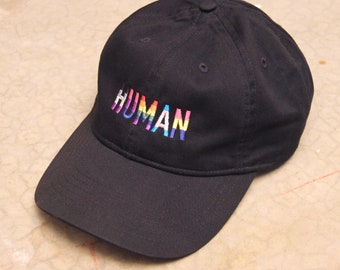 May include: A black baseball cap with a rainbow embroidered "HUMAN" on the front.