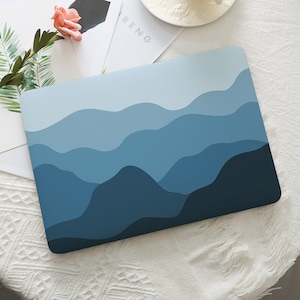 Pode incluir: Um adesivo retangular para portátil com um design de paisagem abstrato em camadas, apresentando ondas suaves e onduladas em vários tons de azul, variando de um azul-celeste claro no topo a um azul-marinho profundo na borda inferior.