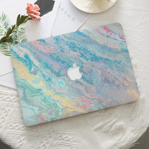 May include: A laptop skin featuring a marbled design in shades of blue, pink, yellow, and white. The skin has a subtle shimmer and a contemporary, abstract look.