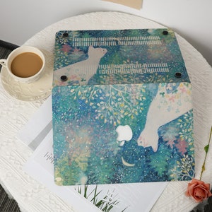 May include: A laptop skin with a watercolor design featuring two white cats, a crescent moon, and a starry night sky. The design is in shades of blue, green, and pink, with a white background. The skin is designed to fit a MacBook Pro.