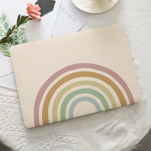 May include: A beige laptop case featuring a colorful rainbow design. The rainbow arcs are in shades of pink, yellow, green, and blue. The case is on a white surface with a flower and greenery in the background.