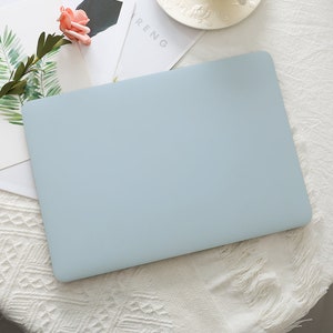 May include: A light blue laptop case. The case is rectangular with rounded corners. The case is on a white surface with a floral arrangement and a magazine.