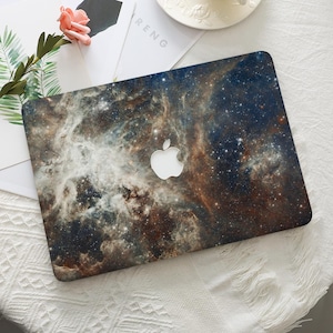 May include: A laptop skin featuring a detailed nebula print with deep blue, brown, and white cosmic clouds and scattered stars. The design covers the rectangular lid of the device, which displays a centered, silver-colored Apple logo cutout.