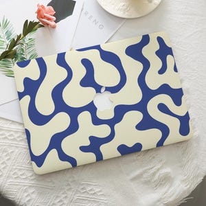 May include: A laptop case with a cream-colored background and a pattern of navy blue organic shapes. The Apple logo is visible in the center. The case is on a white surface.