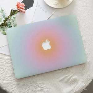 May include: A laptop hard shell case featuring a soft gradient design that transitions from a pale mint green at the edges to a warm orange and pink centre. The case has a precise cutout in the middle to reveal the silver Apple logo underneath.