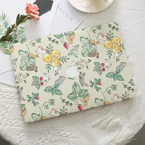 Op de afbeelding: Een laptophoes met een crèmekleurige achtergrond met een patroon van konijntjes, gele bloemen, aardbeien en groene bladeren. De hoes heeft een uitsparing voor het Apple-logo.