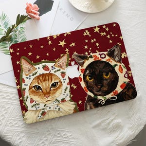 Peut inclure: Une coque rigide pour ordinateur portable sur fond rouge foncé parsemé d'étoiles dorées. Le motif représente un chat tigré orange et un chat noir, portant tous deux des bonnets blancs ornés de petites fraises rouges et de motifs de fruits.