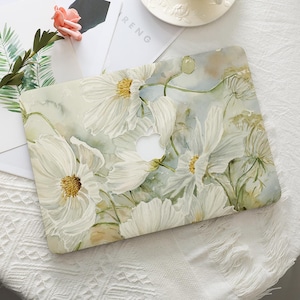 May include: A laptop case with a watercolour floral design. Large white flowers with yellow centres are set against a light green and blue backdrop. The Apple logo is visible. The word "RENG" is visible on a piece of paper.