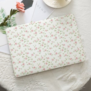 May include: A white laptop case with a delicate floral pattern of pink roses and green leaves. The design covers the entire surface, creating a cohesive and elegant look. The case is likely made of a durable material to protect the laptop.