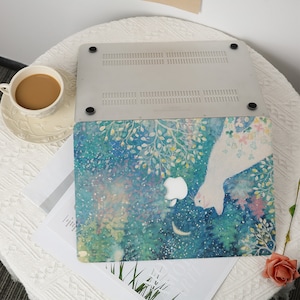 May include: A laptop with a blue, green, and white watercolor design. The design features a white cat, a crescent moon, and a starry sky. The laptop is closed and the design is on the top of the laptop.