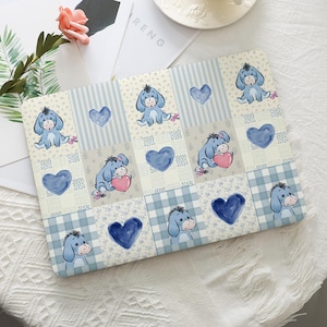 May include: A rectangular laptop skin featuring a patchwork design of light blue and cream squares. The pattern includes illustrations of a blue donkey character, watercolor-style blue hearts, and small floral motifs on striped and checkered backgrounds.
