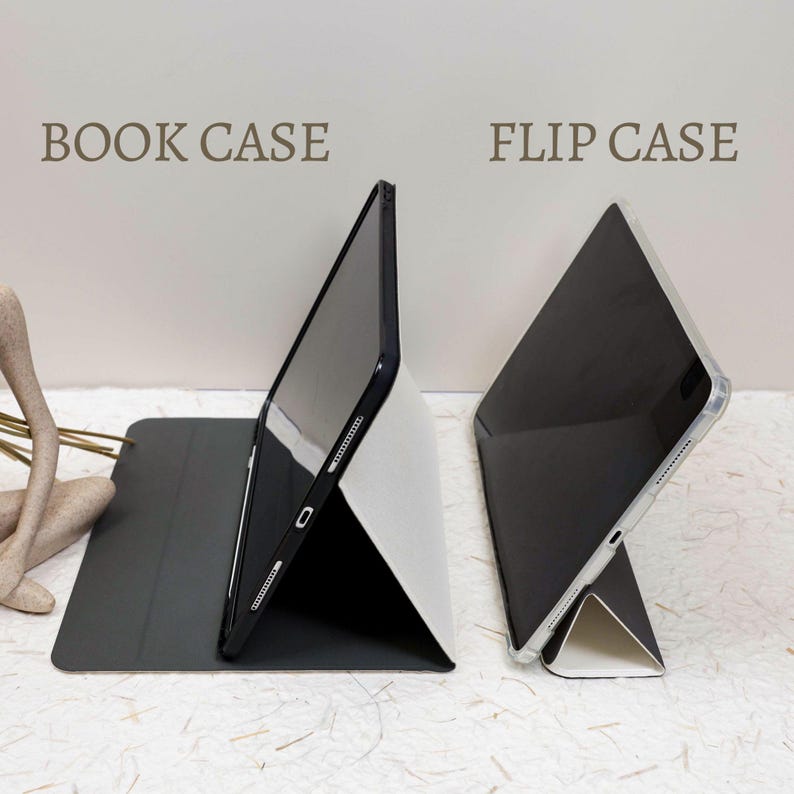 May include: A black book case and a flip case for a tablet are displayed side by side. The book case features a dark cover and a stand, while the flip case has a clear shell and a white stand. Both cases are shown in a propped-up position.