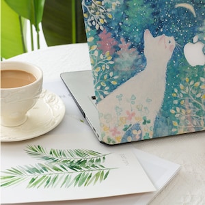 May include: A laptop computer with a blue and green watercolor design featuring a white cat and the word 'NATURE'. The design includes flowers and leaves. The laptop is sitting on a white surface with a cup of coffee and a piece of paper with a green plant design.