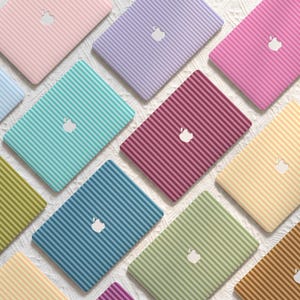 May include: A collection of laptop skins featuring a variety of pastel and vibrant colours, each with a consistent vertical striped pattern and a central white Apple logo cutout. The skins are arranged in a grid-like layout, showcasing colours including pink, lavender, magenta, teal, yellow, olive green, and blue.