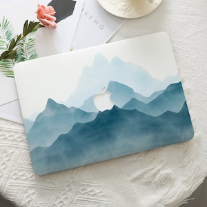 Op de afbeelding: Een witte laptophoes met een blauw aquarel bergontwerp. Het Apple-logo is zichtbaar op de hoes.