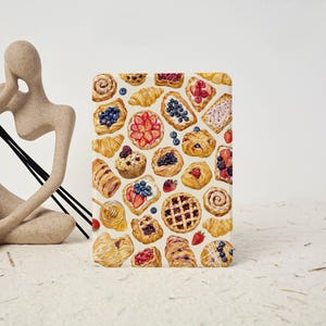 May include: A rectangular tablet case featuring a detailed, colorful illustration of various baked goods, including croissants, fruit tarts, danishes, and muffins topped with blueberries, strawberries, and raspberries, arranged on a light background.
