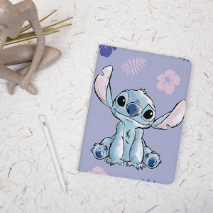 May include: A light purple tablet case featuring a cartoon illustration of Stitch from Lilo & Stitch. The case has a floral and leaf pattern. A white stylus is next to the case.
