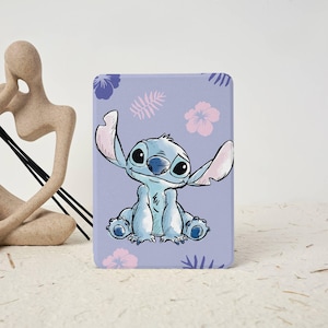 Può includere: Una custodia rettangolare viola chiaro con un'illustrazione a cartoni animati di Stitch di Lilo & Stitch. Il personaggio blu ha grandi orecchie e occhi, con accenti floreali e di foglie rosa e viola. La custodia è probabilmente per un tablet o un e-reader.
