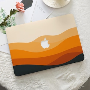 Può includere: Una custodia per laptop con un design ispirato al tramonto. La custodia presenta strisce orizzontali arancioni, gialle e verde acqua scuro. Il logo Apple è visibile. La custodia è su una superficie bianca.