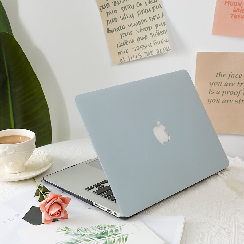 May include: A light blue laptop with the Apple logo on the lid is open on a white surface. A cup of coffee, a rose, and some papers are nearby. The text on the paper says "There are still so many kisses and laughs and nights and days and risks worth taking and proud trips and books to read and".