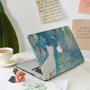 May include: A laptop computer with a white cat design on the lid. The design is a watercolor painting of a white cat looking up at a crescent moon in a blue sky with white stars. The cat is surrounded by green and pink flowers and leaves. The laptop is open and the keyboard is visible. The laptop is sitting on a white surface with a cup of coffee and a rose on the left side of the laptop.