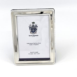 Puede incluir: Marco de fotos de plata con un borde de cuentas. El marco tiene un pequeño escudo con el texto "Arl D. Norman London" y el texto "Hallmarked Sterling Silver made in England". El marco está diseñado para albergar una foto de 3 1/2 pulgadas por 2 1/2 pulgadas.