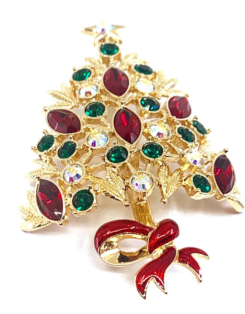 May include: Gold-coloured Christmas tree brooch with red, green, and clear gemstone accents. The brooch features a red enamel bow at the base and a star at the top. A festive holiday accessory.