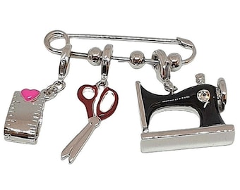 May include: Silver charm bracelet with three charms: a sewing machine, a pair of scissors, and a measuring tape with a pink heart. The charms are attached to a silver safety pin.