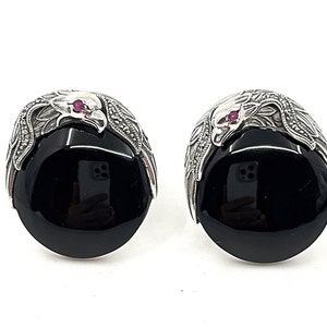 May include: A pair of silver earrings with black onyx stones and a detailed eagle design. Each eagle has a small red gemstone for an eye.