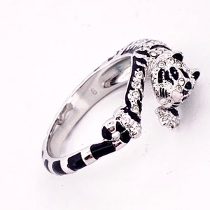 Könnte beinhalten: Ein silberner Ring mit einem schwarzen und weißen Emaille-Design einer Katze mit klaren Strasssteinen. Die Katze ist zusammengerollt, mit dem Schwanz um den Körper gewickelt.