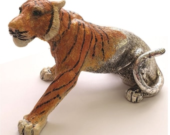 May include: A silver and orange tiger figurine with black stripes. The tiger is lying down with its head turned to the side and its tail curled around its body.