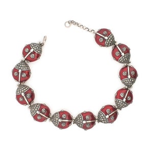 Könnte beinhalten: Ein silbernes Armband mit roten Emaille-Glückskäfer-Anhängern. Jeder Anhänger ist mit schwarzen Markasit-Steinen verziert.