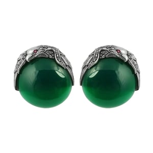 May include: A pair of silver earrings with green gemstone cabochons and red gemstone accents. The earrings feature a detailed eagle design.