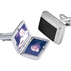 May include: Silver-toned cufflinks with a rectangular design. One cufflink is open, revealing a small photo of a child. The other cufflink has a black rectangular accent. The cufflinks are on a white background.