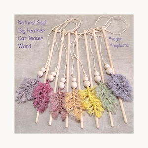 May include: A set of seven cat teaser wands with wooden sticks, each featuring a macrame feather in various colours including grey, pink, yellow, and green, accented with wooden beads and string. Text reads: Natural Sisal Big Feather Cat Teaser Wand #vegan #noplastic.