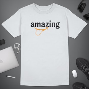 Peut inclure: T-shirt blanc avec le mot "amazing" imprim&eacute; en noir avec un sourire stylis&eacute; Amazon orange.
