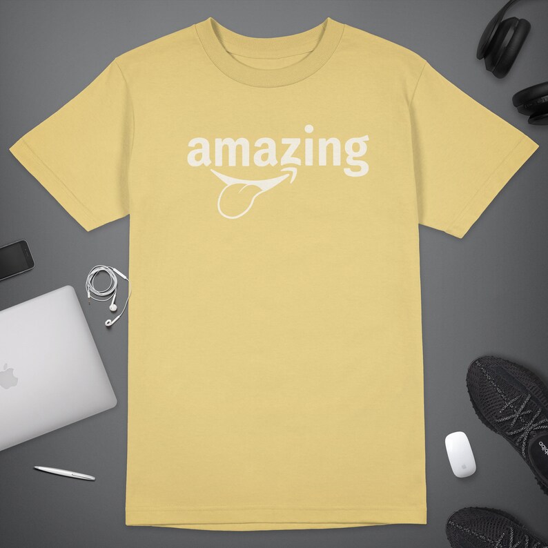 Peut inclure: Un t-shirt jaune avec un graphique blanc d'un visage souriant avec la langue qui sort et le mot "amazing" au-dessus.