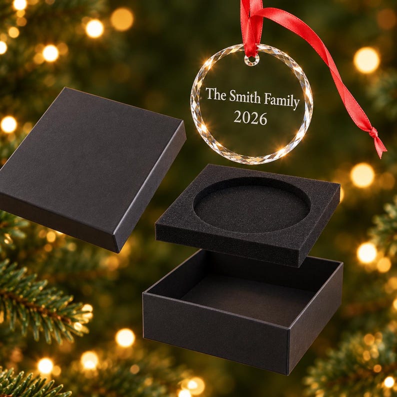 Engraved glass family Christmas bauble reading The Smith Family 2026 with red ribbon above an open black gift box, free gift box included
