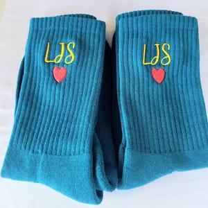 May include: A pair of teal blue socks with the initials "LJS" embroidered in yellow with a red heart above the letters.