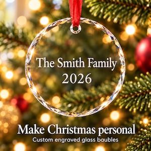 Personalised family Christmas ornament: engraved glass bauble reading The Smith Family 2026 with red ribbon on a lit Christmas tree, custom engraved glass baubles