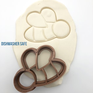 May include: A brown plastic bee-shaped cookie cutter with the words "DISHWASHER SAFE" printed on the white background.