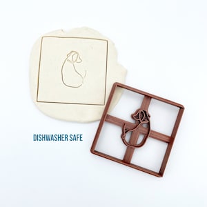 May include: A brown plastic cookie cutter in the shape of a dog. The cookie cutter is on a white surface. The text "DISHWASHER SAFE" is visible below the cookie cutter.