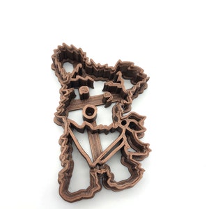 May include: A brown 3D printed cookie cutter shaped like a dog with a hat and a scarf.