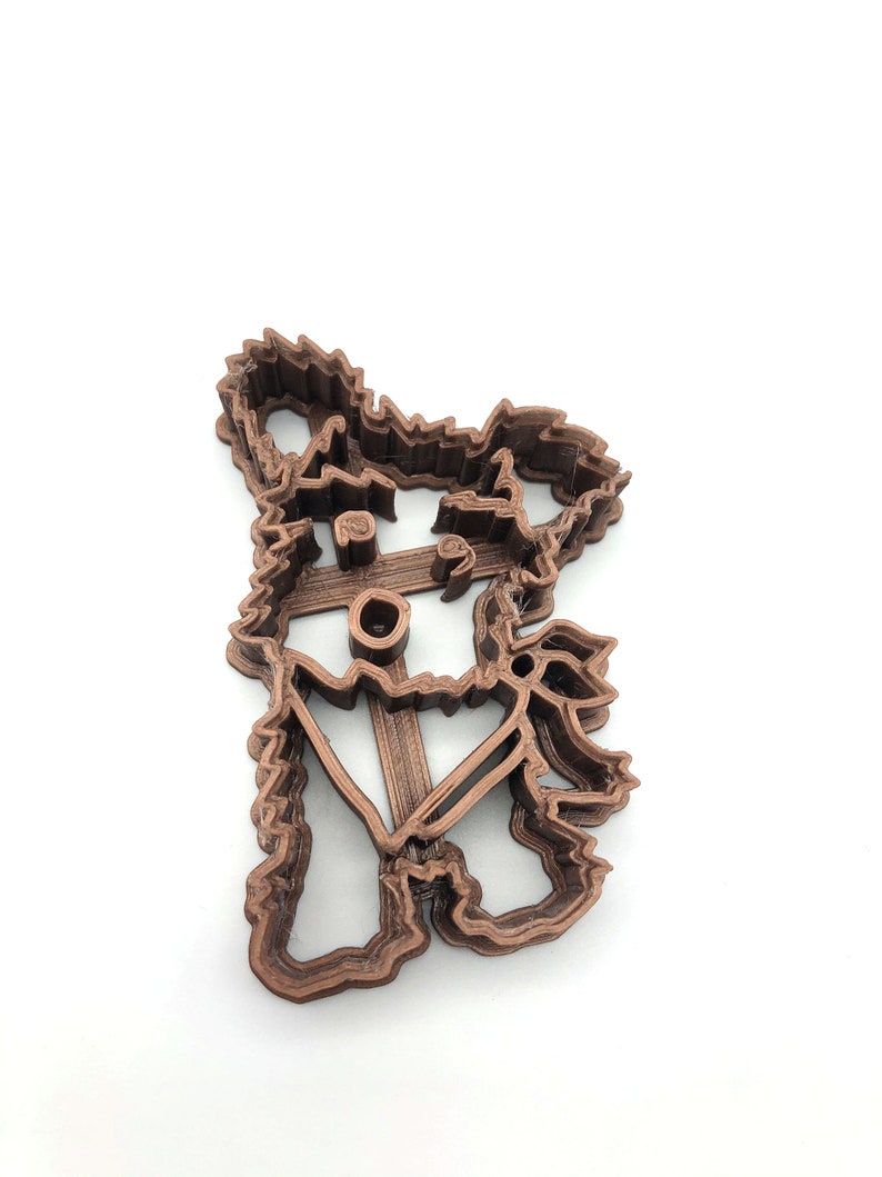 May include: A brown 3D printed cookie cutter shaped like a dog with a hat and a scarf.