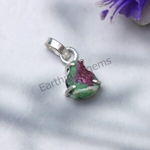 Op de afbeelding: Een zilveren hanger met een ruwe groene en roze edelsteen. De edelsteen is gezet in een zilveren bezel en heeft een ruw, natuurlijk uiterlijk. De hanger is perfect om een ​​toets van natuur aan elke outfit toe te voegen.