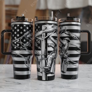 Könnte beinhalten: Ein Edelstahlbecher mit einem schwarz-weißen amerikanischen Flaggenmuster und einer Grafik eines Elektrikers, der an einem Strommast arbeitet. Der Becher hat einen Griff und einen Deckel.