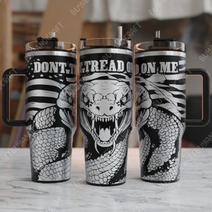 Op de afbeelding: Een set van drie roestvrijstalen bekers met een zwart en zilver ontwerp. De bekers hebben een slang met een Amerikaanse vlag achtergrond en de tekst "Don't Tread On Me".
