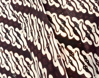 Könnte beinhalten: Eine Nahaufnahme eines weißen und braunen Stoffes mit einem sich wiederholenden Muster aus wellenförmigen Linien und kleinen Quadraten. Der Stoff hat ein traditionelles Batik-Design.