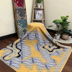 Puede incluir: Una tela estampada en amarillo, azul y negro con un diseño geométrico. La tela está doblada y drapeada sobre una silla.